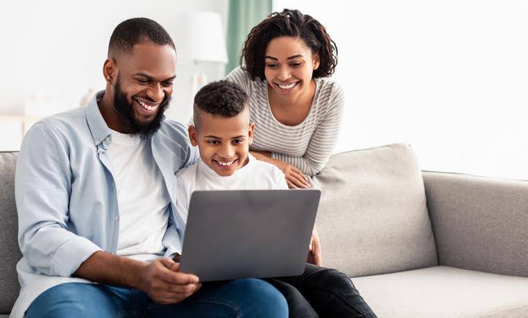 Happy family sitting together looking at a laptop, enjoying comfort from a new AC system.