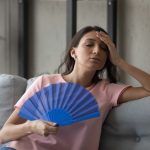 Woman fanning herself with her hand, trying to cool down in a hot room.