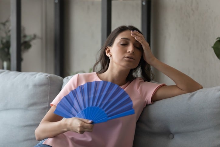 Woman fanning herself with her hand, trying to cool down in a hot room.
